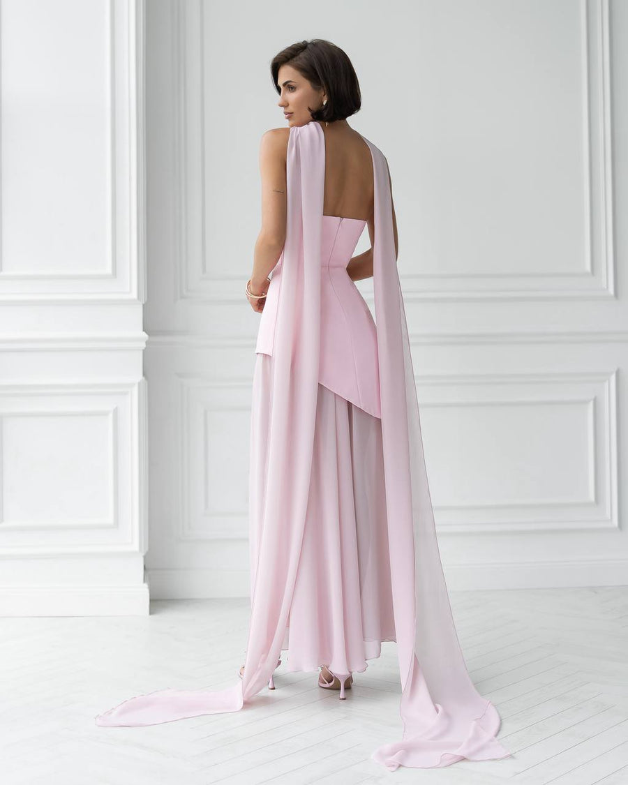 Woman wearing a pink evening gown with a cape in a white room.