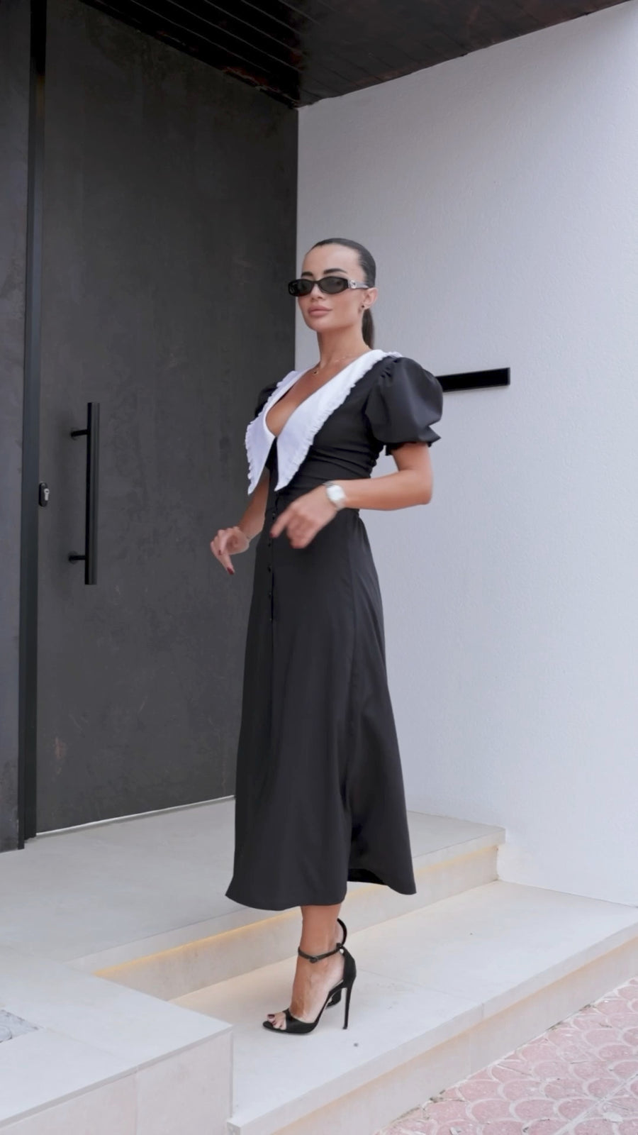Woman in a black dress with white accents standing on steps outside a building.