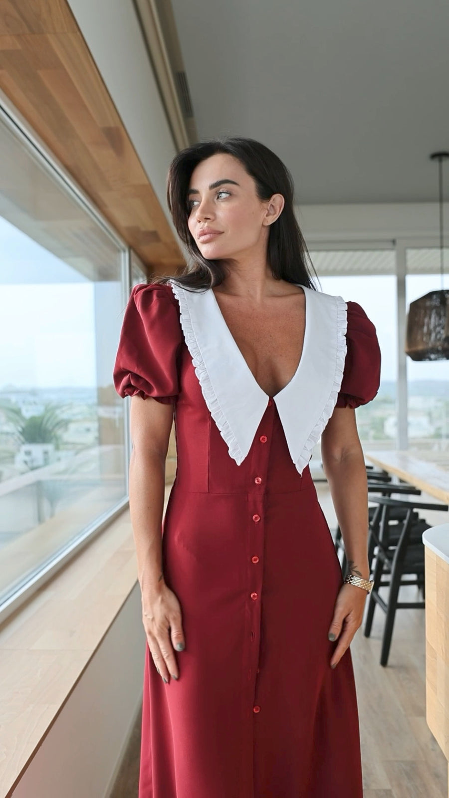Woman in a red dress with white collar standing in a modern interior setting.