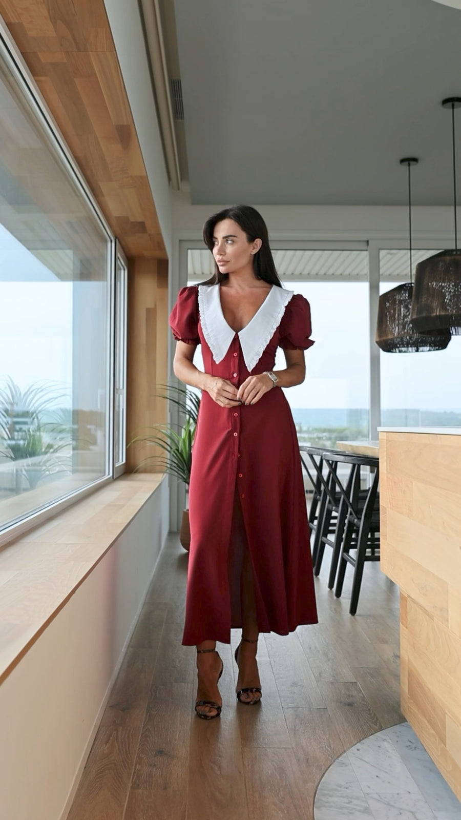 Woman in a red dress standing in a modern interior setting with large windows.