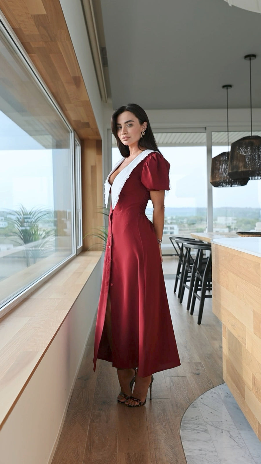 Woman in a red dress standing in a modern interior setting with large windows.