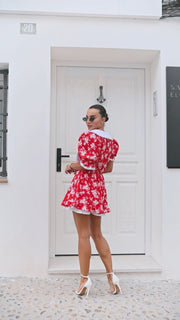 Woman in a red floral dress standing in front of a white door.