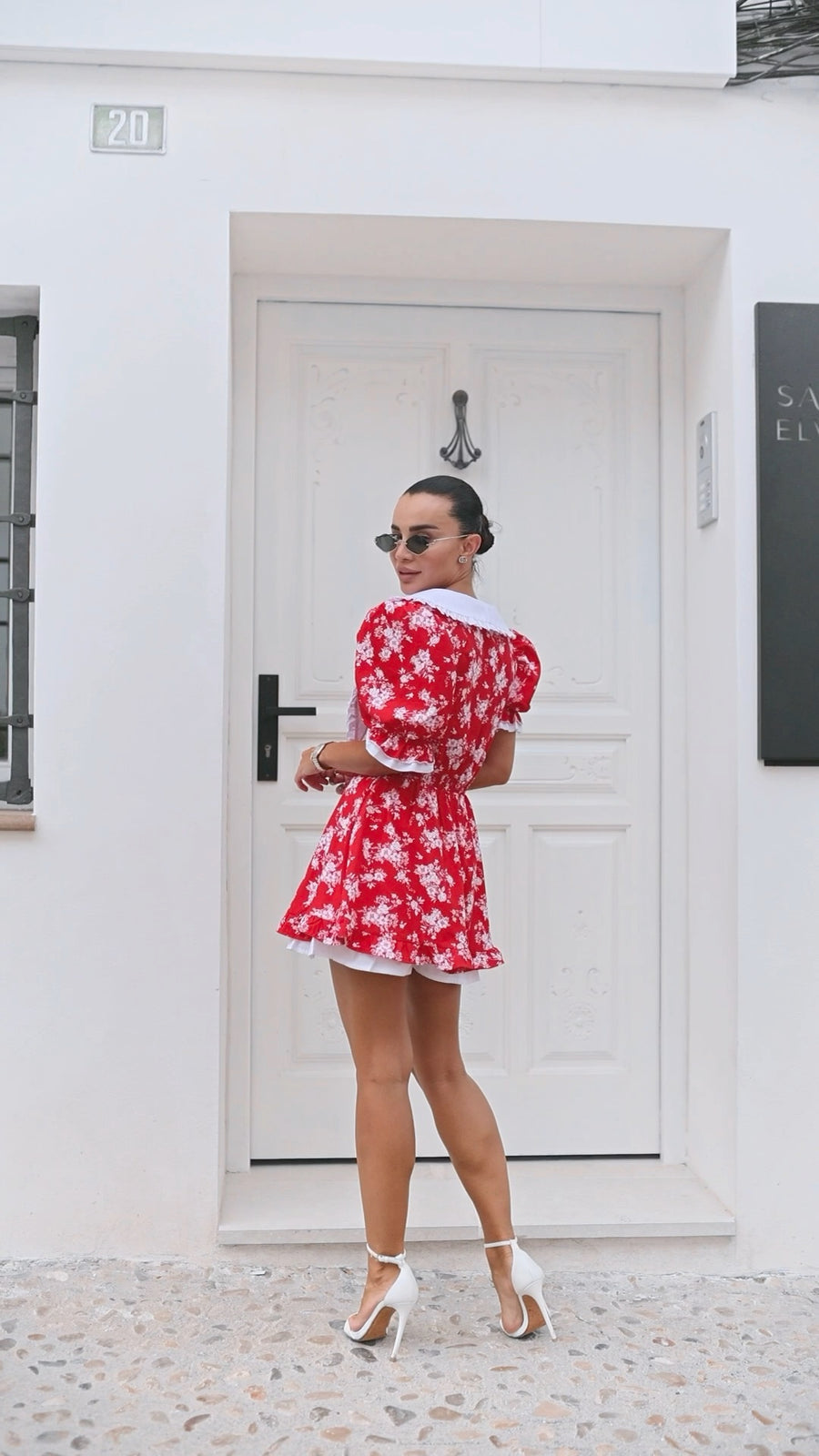 Woman in a red floral dress standing in front of a white door.