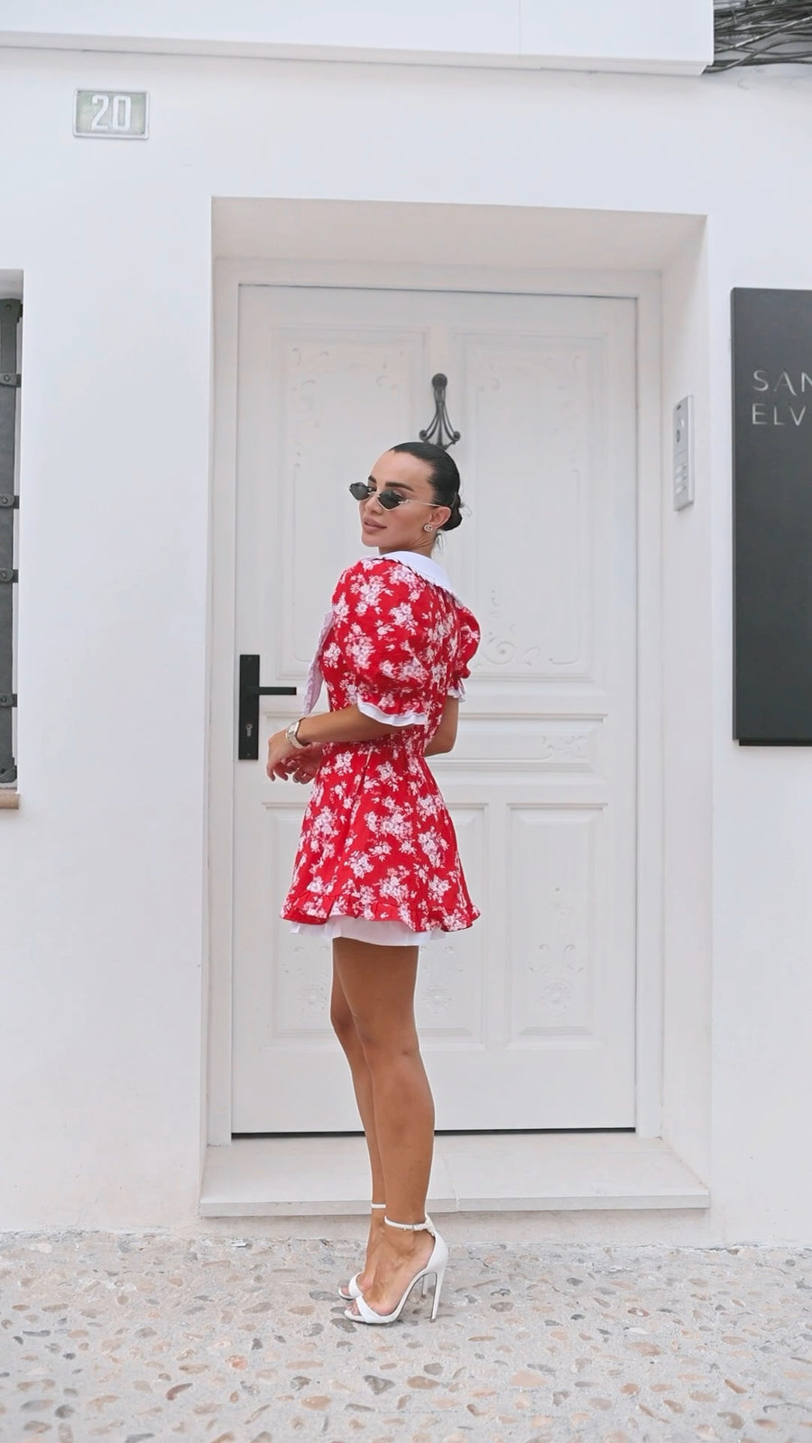 Woman in a red floral dress standing in front of a white door.