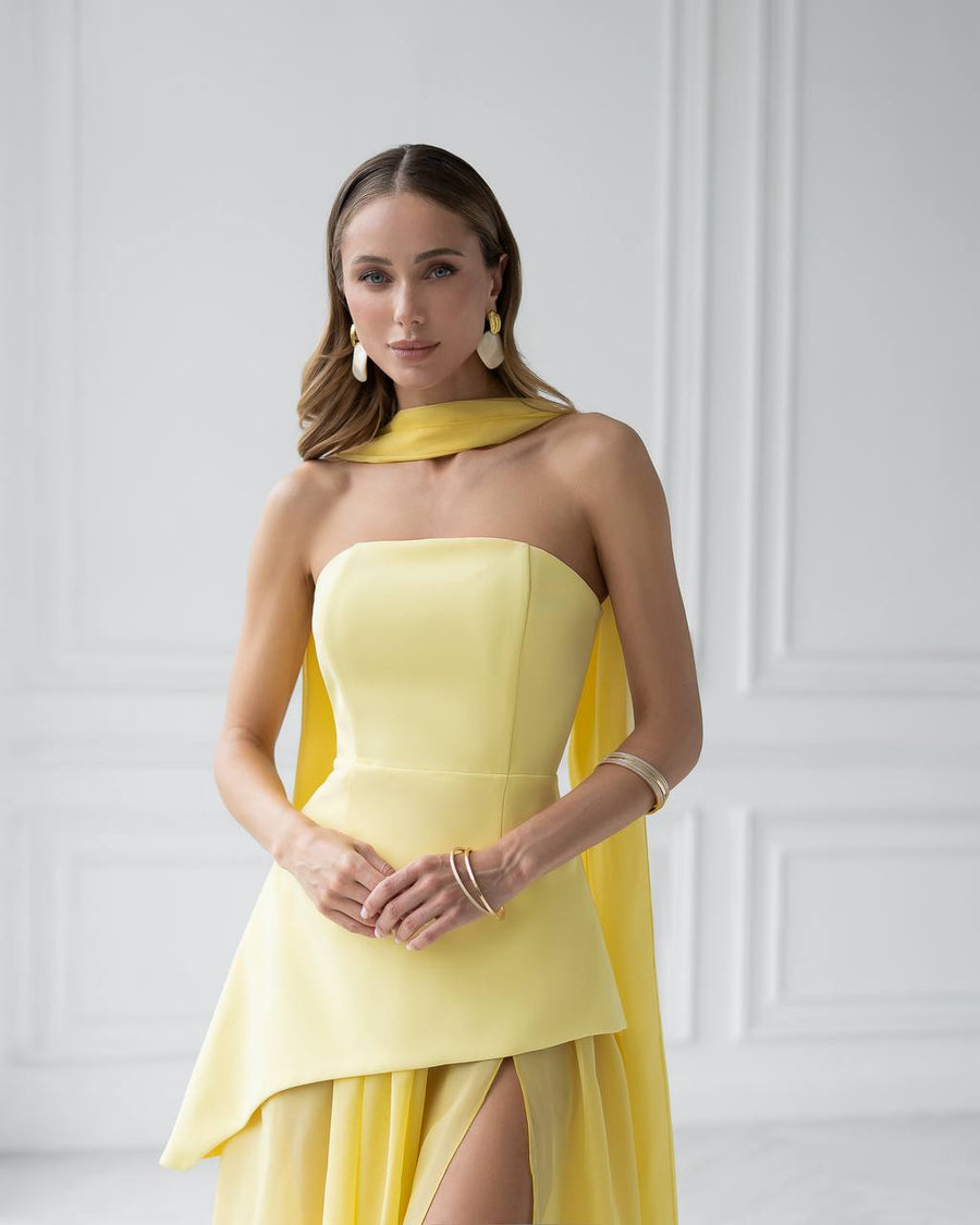 Woman wearing a yellow strapless dress with a slit on a white background