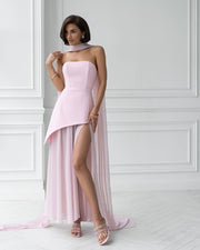 Woman wearing a pink strapless dress with a high slit in a white room.
