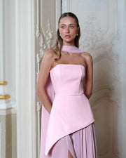 Woman wearing a pink strapless dress with a high-low hem against a decorative wall.