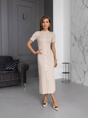 Woman in a beige dress standing in a modern interior setting with gray walls and a marble wall.