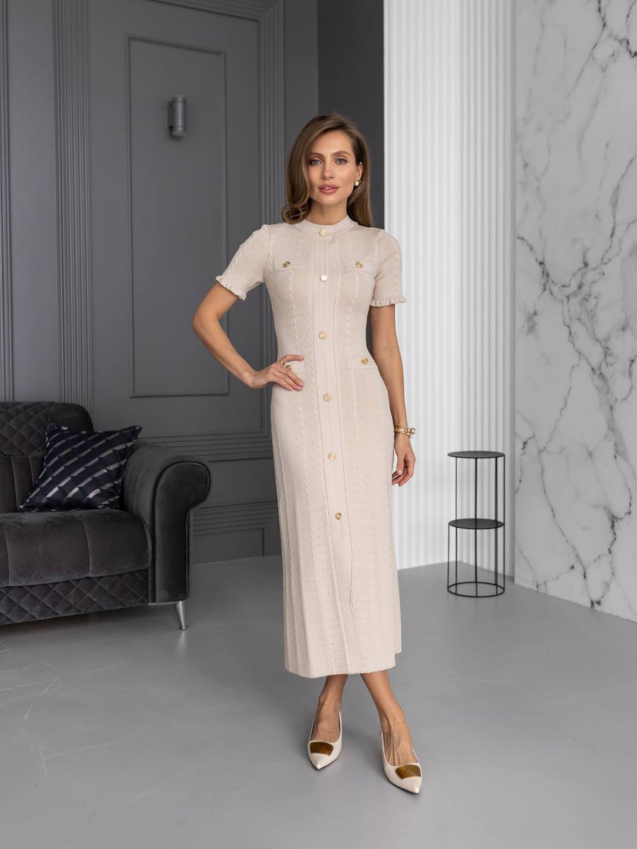 Woman in a beige dress standing in a modern interior setting with gray walls and a marble wall.