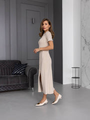 Woman in a beige dress standing in a modern room with gray walls and a dark sofa.