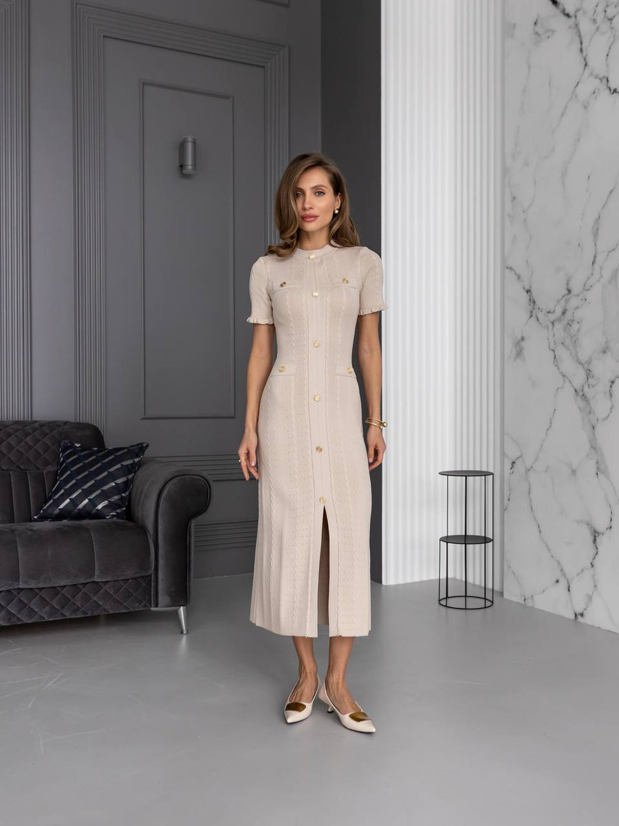 Woman in a beige dress standing in a modern room with gray walls and a marble wall.