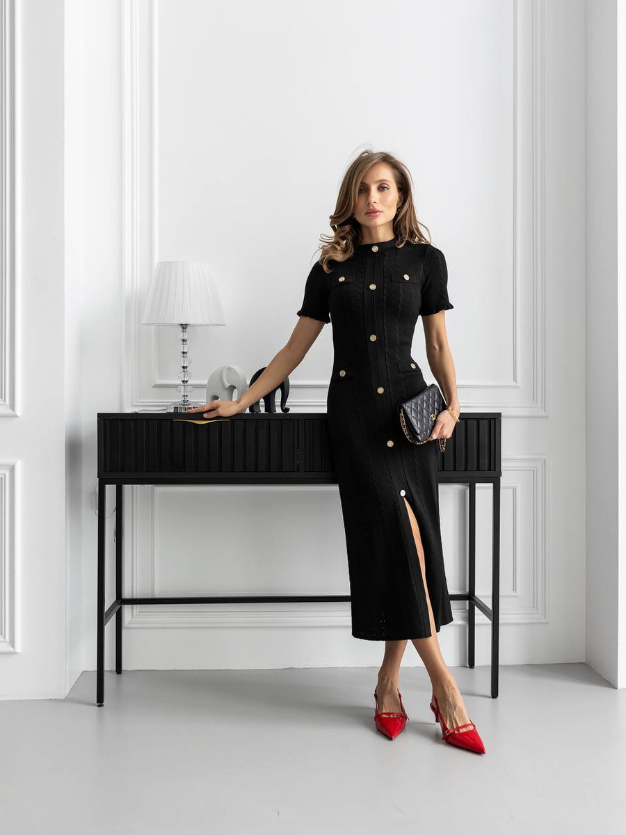 Woman in a black outfit with red shoes standing in a modern interior setting.