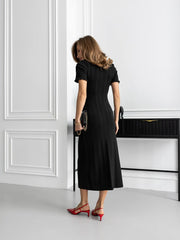 Woman in a black dress standing in a room with white walls and a black console table.