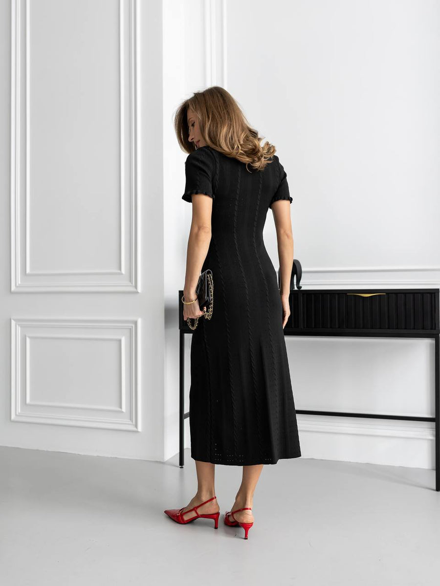 Woman in a black dress standing in a room with white walls and a black console table.