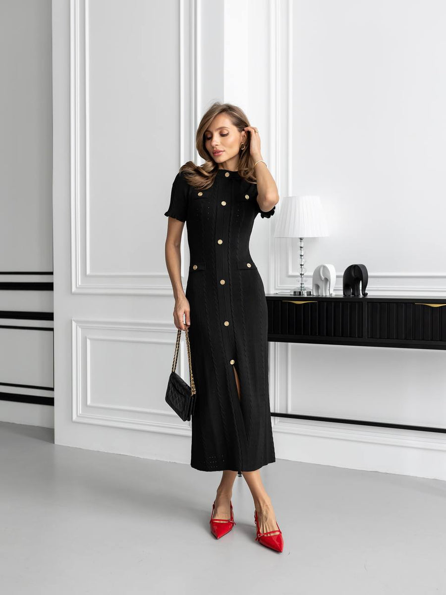 Woman wearing a black dress with gold buttons in an elegant room.