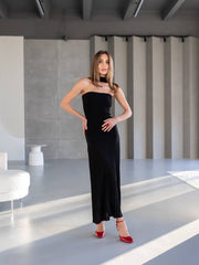 Woman in a black strapless dress with red shoes standing in a modern indoor setting.