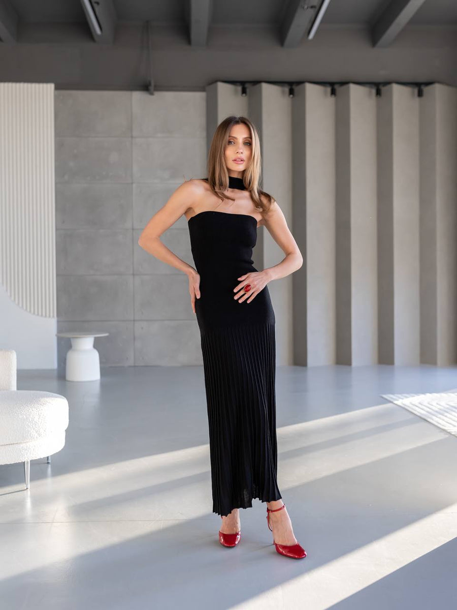 Woman in a black strapless dress with red shoes standing in a modern indoor setting.