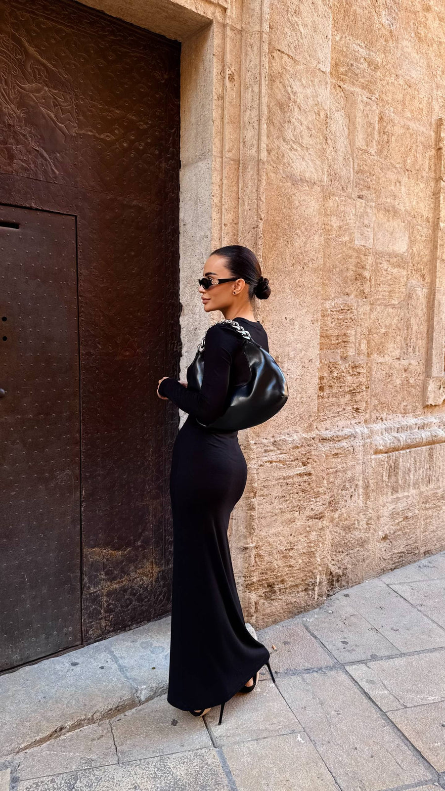 Woman in a black dress standing against a textured wall.