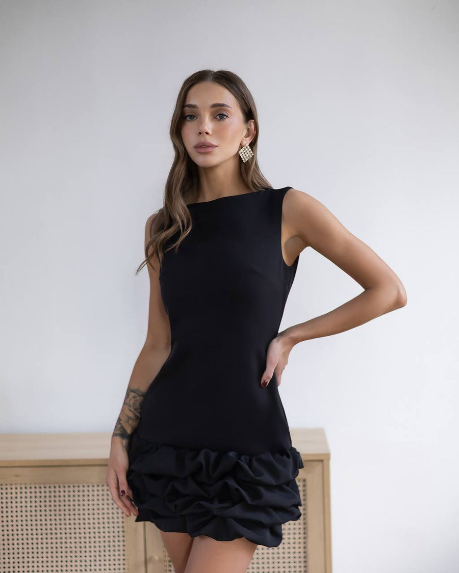 Woman wearing a black dress with ruffled bottom half against a white background