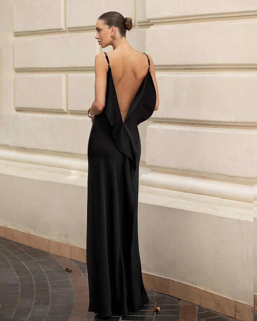 Woman in a black evening gown with a low back standing against a classical architecture wall.