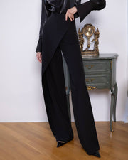 Person wearing a black outfit with wide-leg pants in a room with a wooden floor and a decorative cabinet.