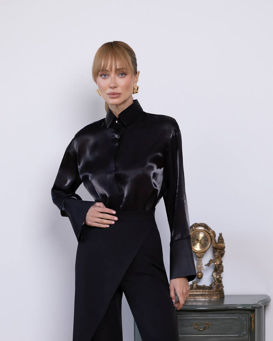 Woman wearing a black satin shirt and black pants against a white background