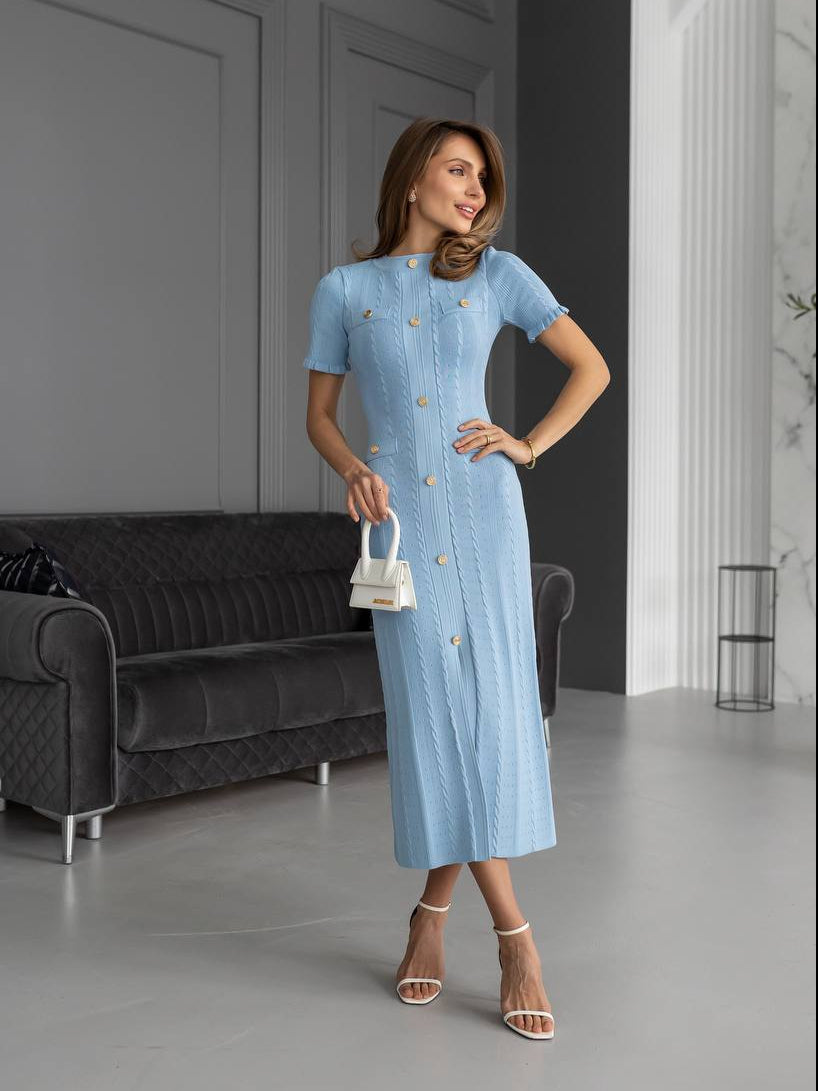 Woman in a light blue dress standing in a modern room with gray walls and a black sofa.