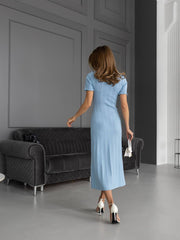 Woman in a light blue dress walking in a modern room with gray walls and furniture.