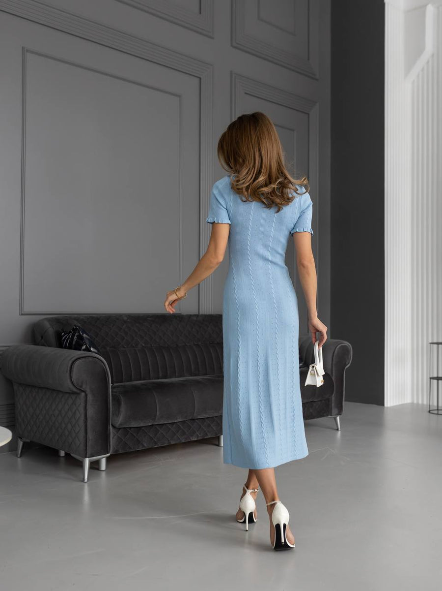 Woman in a light blue dress walking in a modern room with gray walls and furniture.