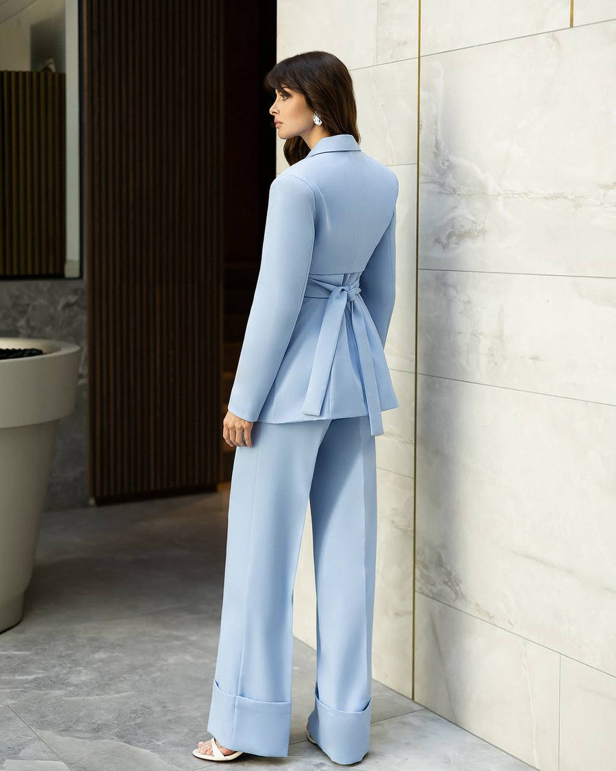 Woman in a light blue suit standing against a tiled wall.