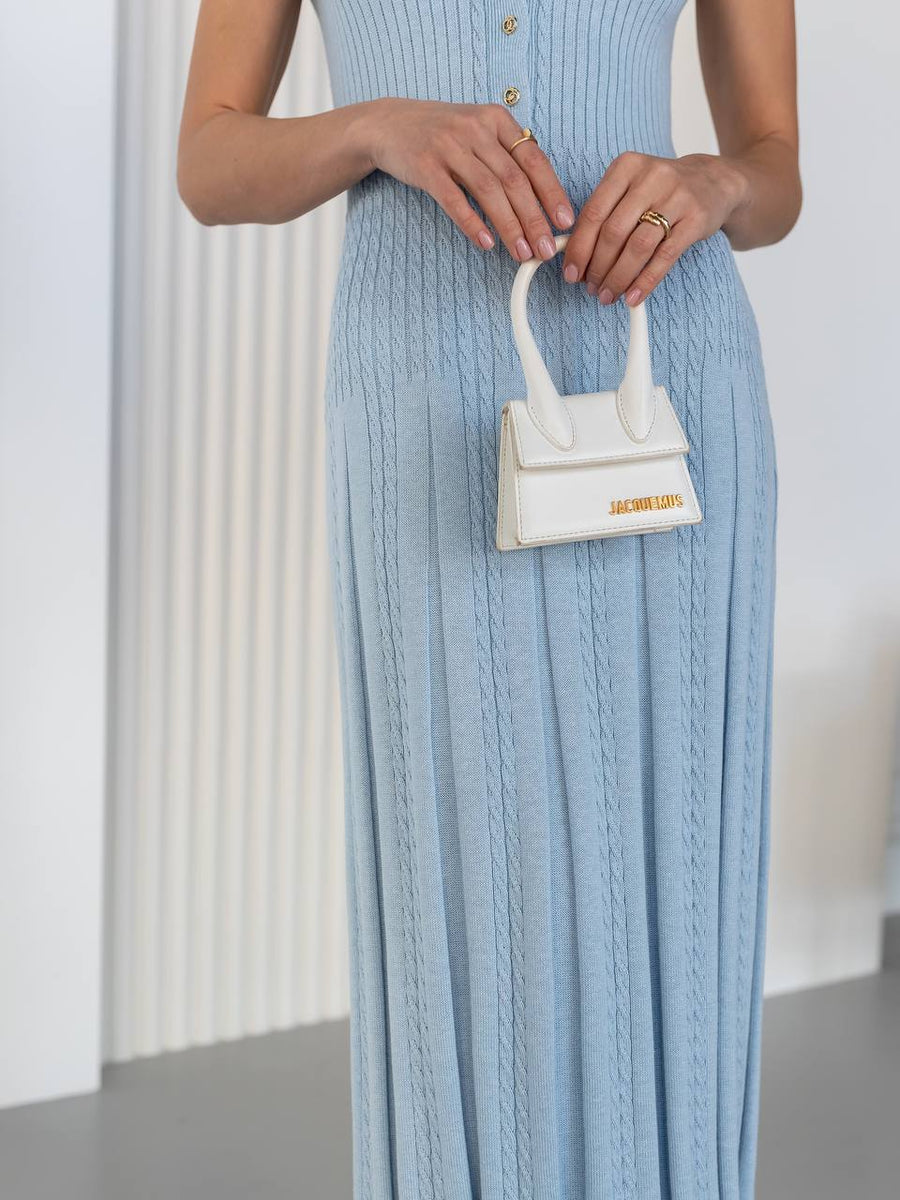 Woman in a light blue dress holding a white handbag with gold accents.