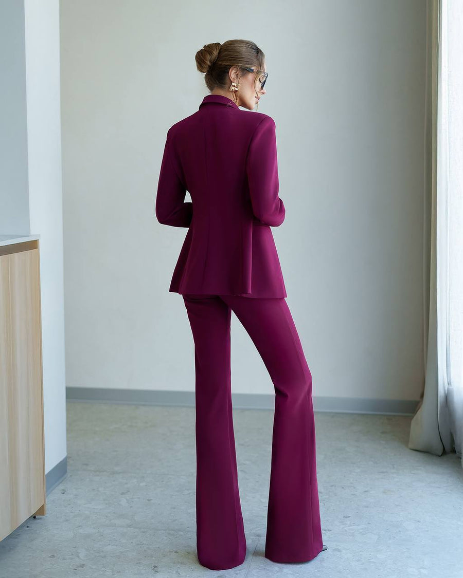 Woman wearing a magenta suit standing in a minimalistic room.