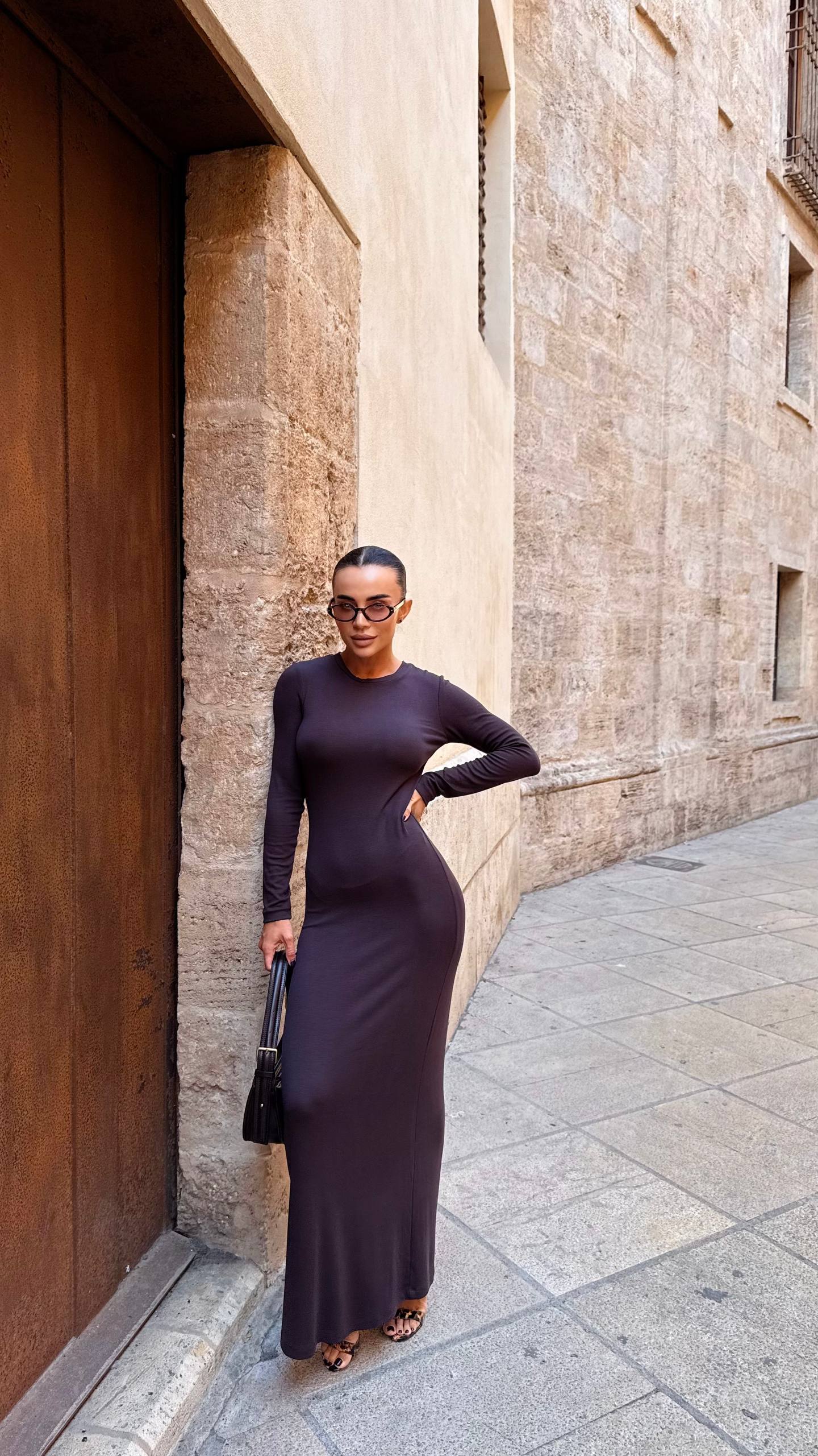 Woman in a long dark dress standing against a stone wall.