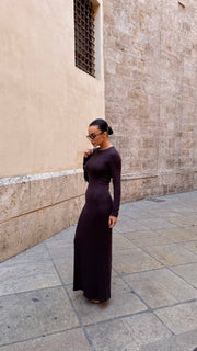 Woman in a long dark dress standing against a textured wall.