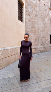 Woman in a black dress standing on a stone pavement against a stone wall.