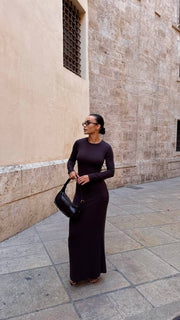 Woman in a long black dress standing against a stone wall.