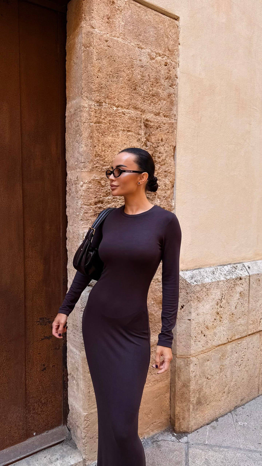 Woman in a black dress standing against a stone wall.