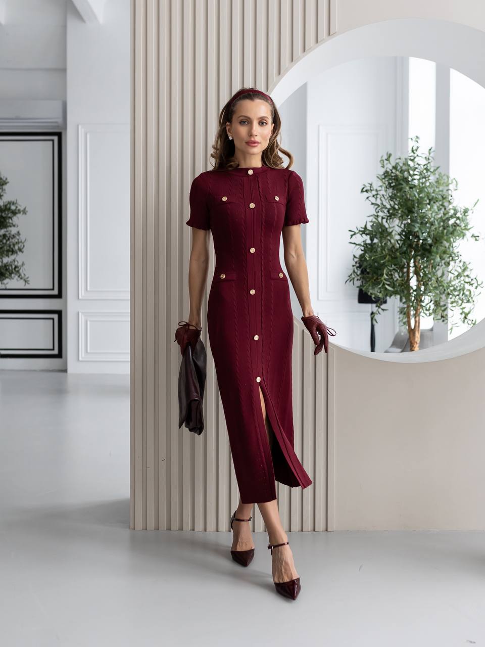 Woman wearing a burgundy dress with white buttons in a modern interior setting.