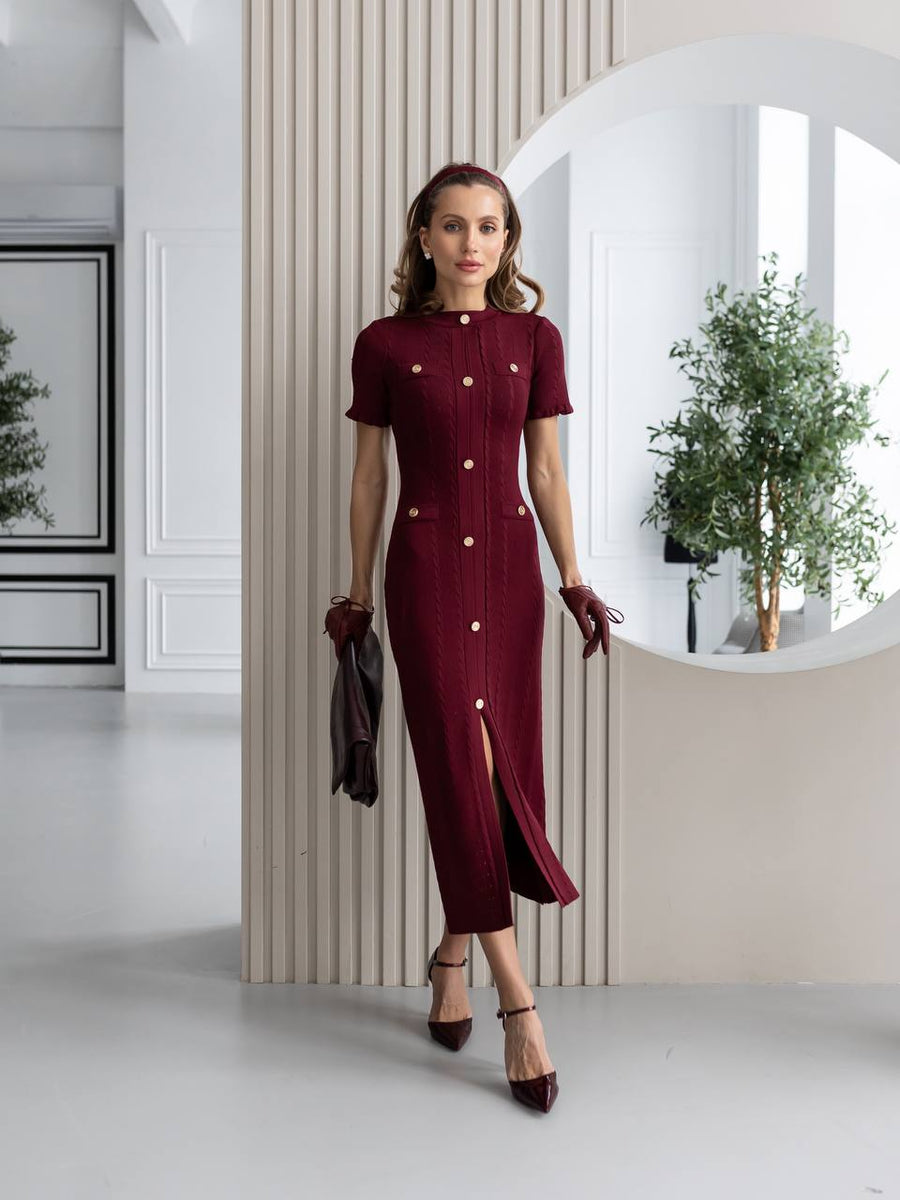 Woman wearing a burgundy dress with white buttons in a modern interior setting.