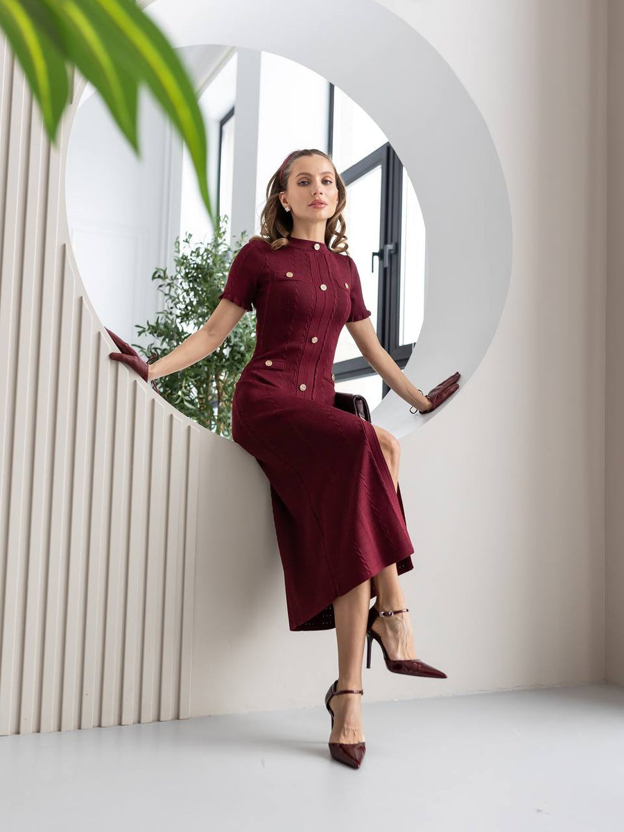 Woman in a burgundy dress sitting on a white wall with a plant in the background