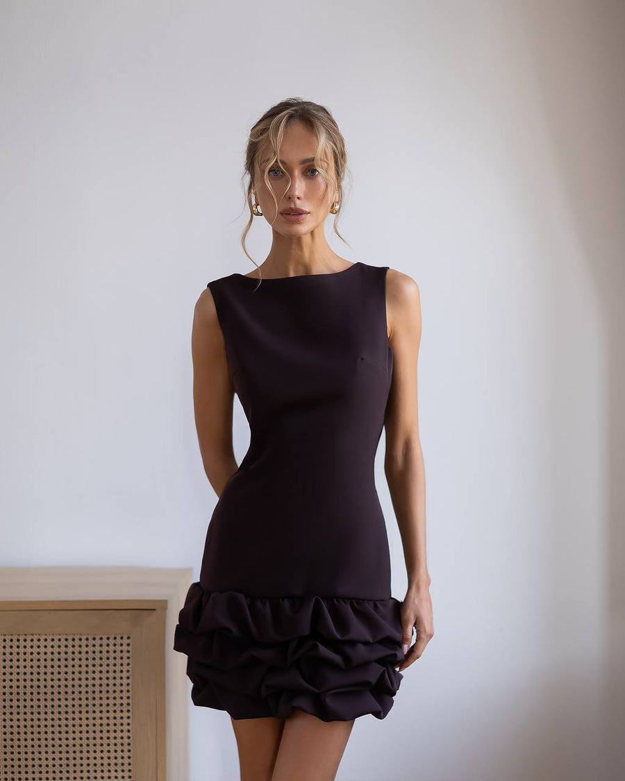 Woman wearing a brown dress with ruffled hem against a plain background