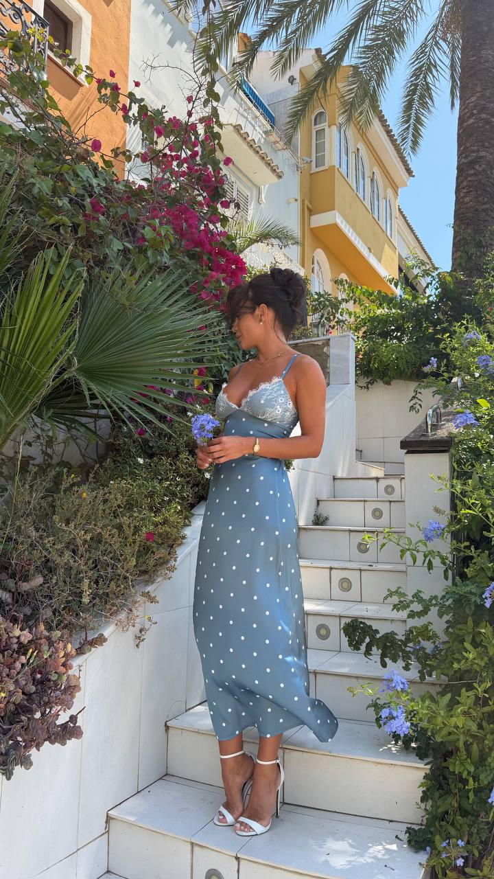 Woman in a blue dress standing on steps with flowers and a building in the background