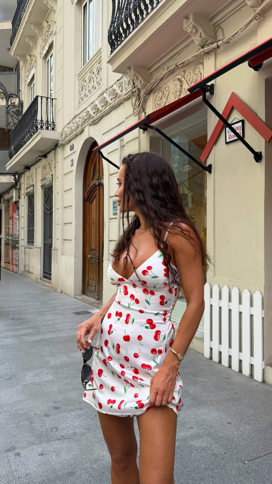 Woman in a white dress with red patterns walking on a street.