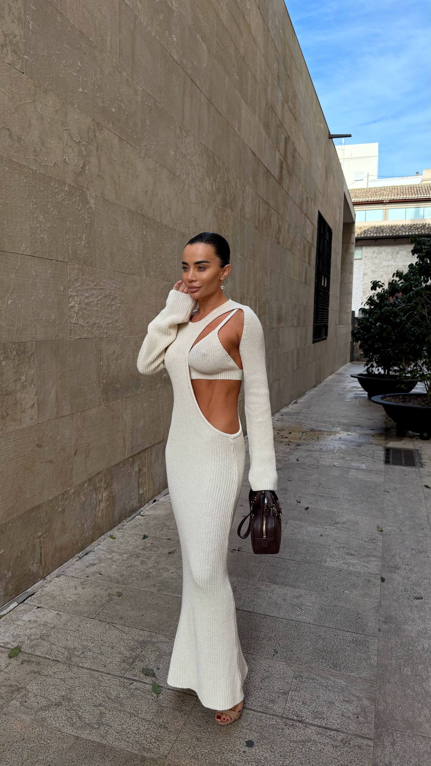 Woman in a white outfit standing against a beige wall with a clear blue sky.