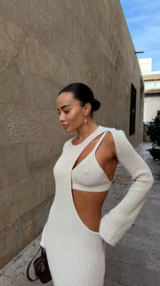 Woman wearing a white ribbed knit dress with cut-out design against a beige wall.