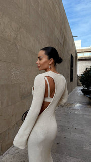 Woman in a white ribbed dress with cut-out design standing against a beige wall.