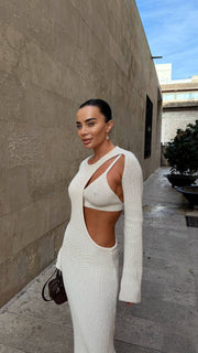 Woman in a white outfit standing against a building with a clear sky.