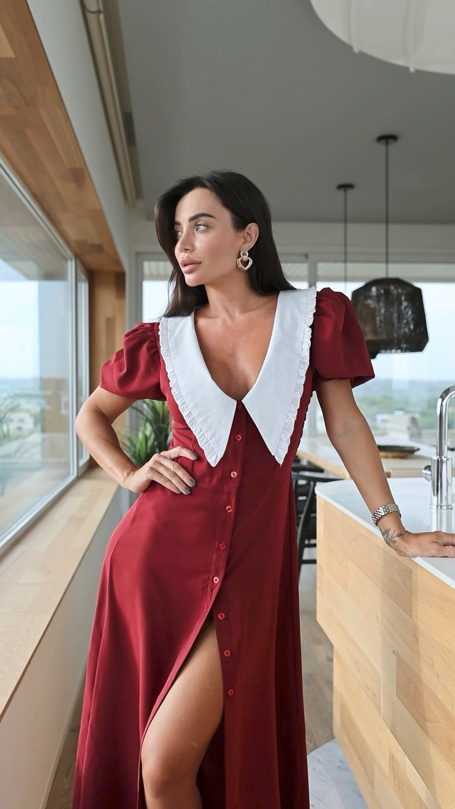 Woman in a red dress with a white collar standing in a modern kitchen.