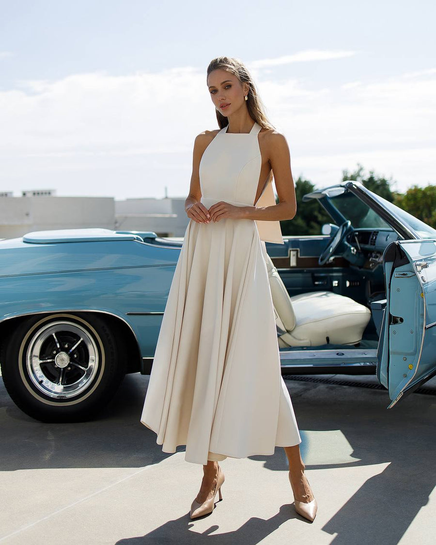 Woman in a white dress standing next to a vintage blue car.