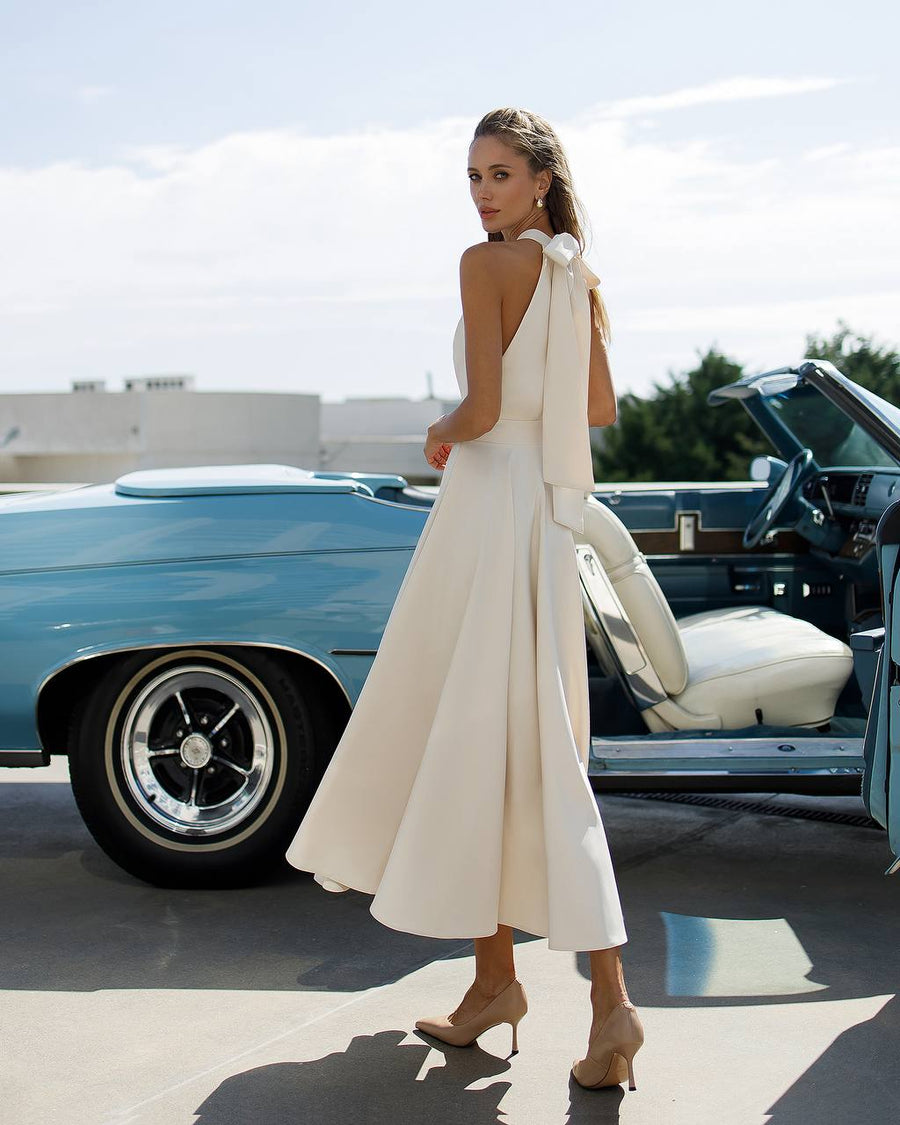 Woman in a white dress standing next to a classic blue car